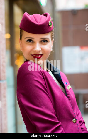 Junge attraktive Frauen arbeiten als Flugbegleiter für Qatar Airways auf London Zwischenstopp. Hübsches lächeln, glücklich und warten auf Flug nach Doha. Stockfoto