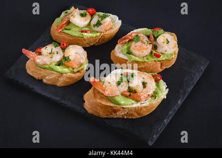 Bruschetta italienische Snacks Sandwiches mit Avocadocreme und Garnelen dekoriert von Petersilie und Paprika. Stockfoto