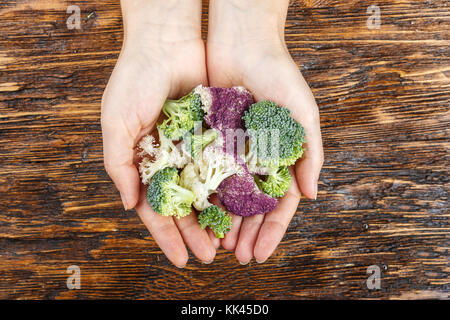 Blütenstände von bunten Blumenkohl - Weiß und Violett und Brokkoli in die Hände eines Mädchens auf einer hölzernen Hintergrund Stockfoto