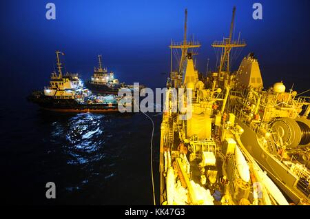 Schlepper ziehen das Minen-Gegenmassenschiff USS Devastator MCM 6, links vom Military Sealift Command, Chartered M/V Tern, ein Float-on/Float-off-Transportschiff, Bahrain, 2012. Bild mit freundlicher Genehmigung der U.S. Navy Foto von Mass Communication Specialist 1st Class Jayme Pastoric/US Navy. Stockfoto