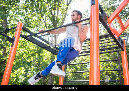 Starker junger Mann dabei erstaunliche Pull-up-Variante bei extremen Stockfoto