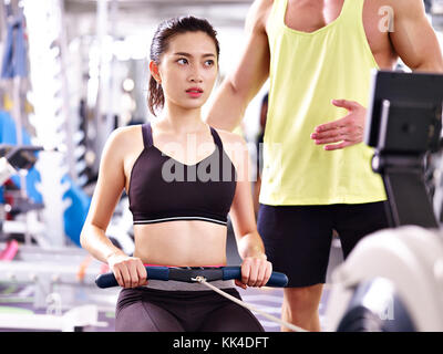 Junge asiatische Frau Trainieren mit rudergerät von einem männlichen Trainer trainiert. Stockfoto