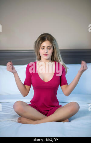 Junge Frau im Bett sitzen, tragen ein rotes Kleid und Meditieren. Stockfoto