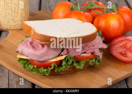 Roastbeef Sandwich mit Salat, Tomate und Käse auf einem Schneidebrett Stockfoto