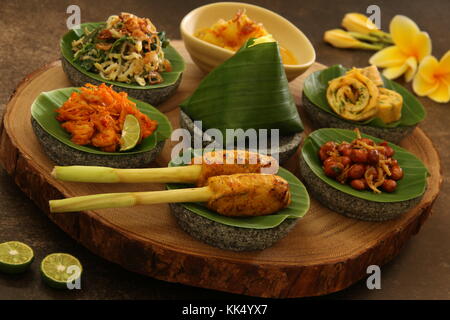 Balinesische Essen Sampler. Verschiedene balinesische Gerichte in kleinen Portionen auf mini Stein Mörser dann auf Holzbrett angeordnet. Stockfoto