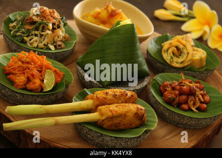 Balinesische Essen Sampler. Verschiedene balinesische Gerichte in kleinen Portionen auf mini Stein Mörser dann auf Holzbrett angeordnet. Stockfoto