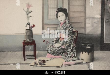 Farbiges Porträt einer jungen japanischen Frau, die kniend, einen Kimono trägt und eine Blume hält, möglicherweise Maiko, eine Lehrgeiko (nicht genau wie Geisha) in Kyoto, Westjapan, 1920. Aus der New York Public Library. Stockfoto