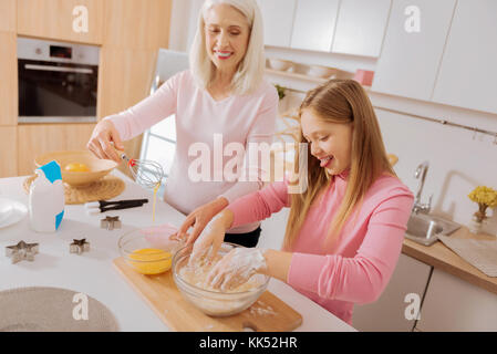 So viel Spaß. freudige glücklich nettes Mädchen mit Blick auf die Schüssel und setzen ihre Hände in Mehl, während Spaß beim Kochen Stockfoto