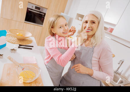 Spaß haben. cute recht glücklich Mädchen berühren ihre Großmütter die Nase und lächelnd, während zusammen mit ihr Stand in der Küche Stockfoto