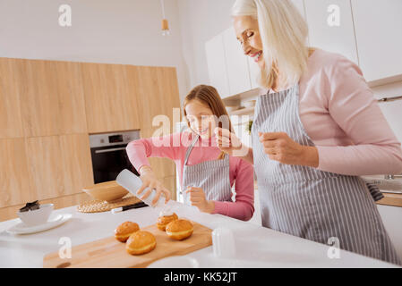 Interessante Tätigkeit. freudige positive nette Großmutter und Enkelin stand in der Küche und gemeinsam Spaß haben beim Kochen Stockfoto