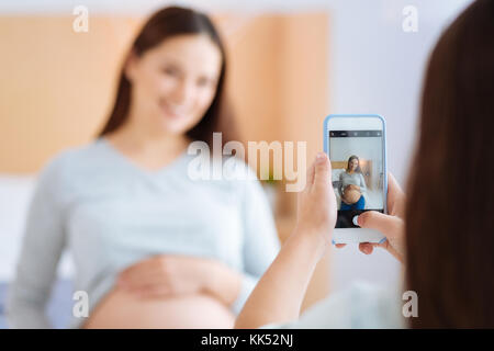 Kaltstufe. selektive Fokus des Telefons mit dem Bild der Sitzung süße schwangere Frau, die ihr der Bauch, die ein Kind unterstützen. Stockfoto