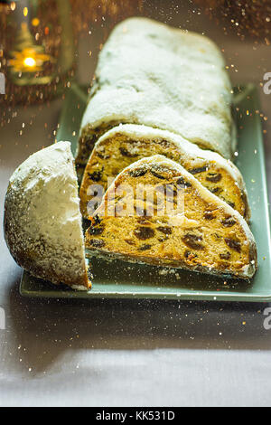 Deutsche Weihnachten Stollen mit Rosinen, Nüssen und kandierten Früchten in Pulverform auf Platte geschnitten Kerzenlicht Sekt bokeh Lichtern festlichen Tisch einstellen Stockfoto