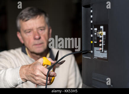 Ältere Menschen schneiden Sie das Kabel auf seinem Kabel-TV-Paket Stockfoto