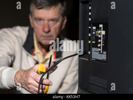 Ältere Menschen schneiden Sie das Kabel auf seinem Kabel-TV-Paket Stockfoto