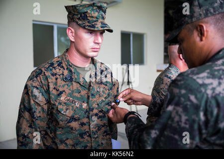 Us Marine Sgt. David G. Gaudette, das Personal noncommissioned Officer verantwortlich für das Honduras Loslösung, Bodenkampf Element, Special Purpose Marine Air-Ground Task Force - Southern Command, ist Pin eines Ausbilders durch einen Honduranischen Marine mit der bataillons de Infanteria de Marina an der Graduierung für die erweiterte Infanterie Kurs in Trujillo, Honduras, 10. November 2017 vorgestellt. Der Kurs wurde entwickelt, um die Fähigkeiten der honduranischen Marines, die die Grundlagen der Infanterie Operationen erarbeitet haben, weiter zu steigern. Die Marinesoldaten und Matrosen von SPMAGTF - SC sind Abschluss ihre Implementierung zu Mittelamerika, d Stockfoto