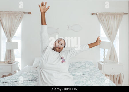 Junge afrikanische Frau Aufwachen im Bett und Stretching Stockfoto