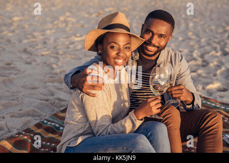 Lächelnden jungen afrikanischen Paar am Strand Wein trinken Sitzen Stockfoto