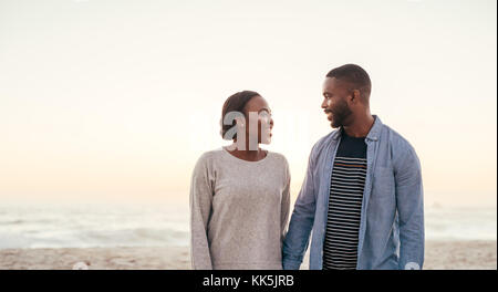 Lächelnd afrikanischen Paar hinunter einen Strand zusammen in der Dämmerung Stockfoto
