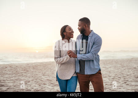 Ein junges afrikanisches Paar, das bei Sonnenuntergang am Strand lacht Stockfoto