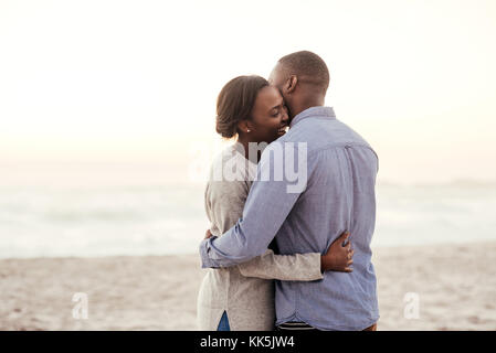 Glückliche junge afrikanische Paar Umarmung an einem Strand in der Dämmerung Stockfoto