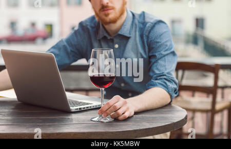 Junge hipster Mann an der Bar im Freien Tisch mit seinem Laptop und mit einem Glas Wein Stockfoto