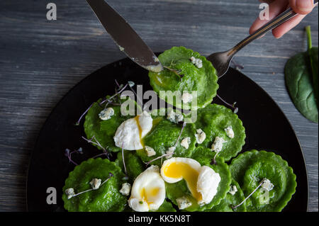 Leckere grüne Ravioli mit Spinat Teig, gefüllt mit Ricotta und Steinpilzen. pochiertem Wachtelei, Blauschimmelkäse. auf einem schwarzen Pla Stockfoto