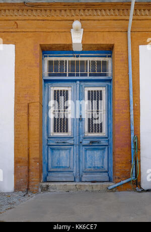 Alte blaue Holztüren bei Cyprian, Dorf. Durch orange gestrichene Wand eingerahmt. Stockfoto