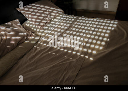 Ungemacht Doppelbett mit Kreis Muster aus dem geschlossenen Shutter. zeigt Schatten von der Sonne. Stockfoto