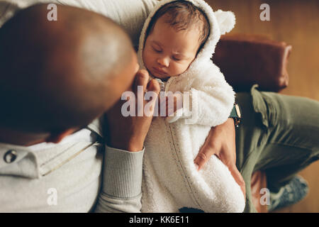 Blick von oben auf den kleinen Jungen, der in den Armen seines Vaters schläft. Neugeborener Sohn mit Vater, der zu Hause auf dem Sofa sitzt. Stockfoto