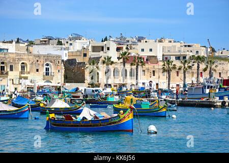 Traditionelle maltesische dghajsa Fischerboote im Hafen mit Uferpromenade Gebäude an der Rückseite, Marsaxlokk, Malta, Europa. Stockfoto