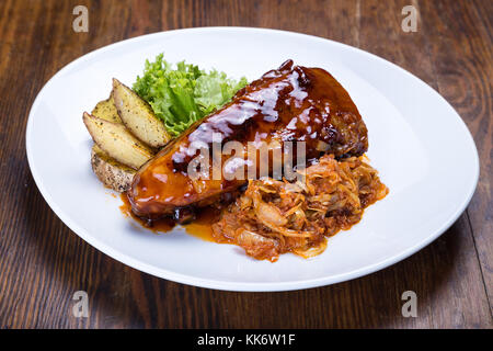 Auf dem Tisch ist eine Platte von gegrillten Rippchen, Sauerkraut, gebackene Kartoffeln und Salat letuk Stockfoto