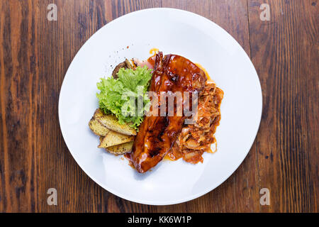 Auf dem Tisch ist eine Platte von gegrillten Rippchen, Sauerkraut, gebackene Kartoffeln und Salat letuk Stockfoto