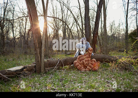 Mann mit Katze Kostüm mit Maske sitzen mit Frau als Hund von Baumstamm in Wald angezogen Stockfoto