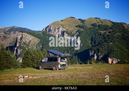 Eine weibliche Camper Zurückbringen zu Ihrem Reisemobil in einem Feld hoch auf einem Hügel über dem Tal Rugova im Kosovo auf einem hellen, sonnigen Tag. Stockfoto