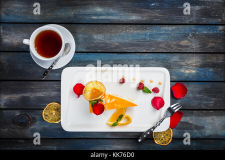 Orange Kuchen mit einer Tasse Kaffee frische Himbeeren auf einer weißen Platte mit Rosenblättern. top anzeigen. schönen hölzernen Hintergrund. Stockfoto