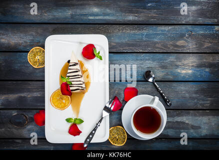 Stück Käsekuchen mit einer Tasse Tee auf einem weißen Teller mit Rosenblättern. top anzeigen. schönen hölzernen Hintergrund. Stockfoto