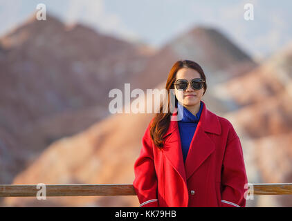 Zhangye, China - Oktober 15,2017: Schöne chinesische Touristen stellt für Ihr Partner mit einem schönen roten Mantel im Inneren der geologische Park von zanghye danxia in China Stockfoto