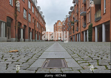 Blick auf eine breite Kopfsteinpflasterstraße mit Reihenhäusern mit roten Backsteinmauern und Reihen von Säulen auf beiden Seiten Stockfoto