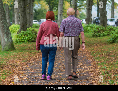 Ältere Paare Wandern entlang eines Pfades im Herbst mit Blätter auf dem Boden in Großbritannien. Stockfoto