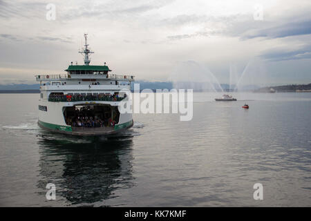 Ein Blick auf die Band und Seahawks Band vom Colman Dock. Ein örtliches Feuerwehrboot nahm an den Festen der Fähre Teil. MV Wenatchee nähert sich Seattle mit dem Feuerboot 30230663084 o Stockfoto