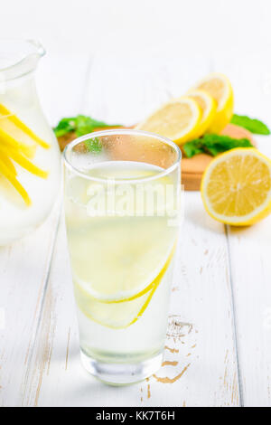 Ein Becherglas und einen Krug kalten Limonade auf einem weißen Hintergrund Holz umgeben von Zitronen Stockfoto