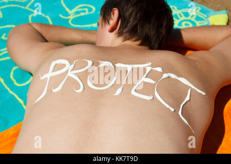 Mann Liegen am Strand und auf dem Rücken mit Sonnencreme schützen geschrieben. Stockfoto