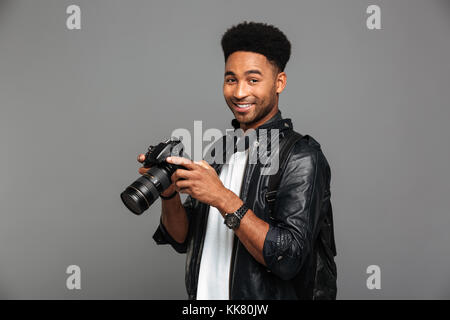 Close-up Portrait von lächelnden afrikanischen Fotografen holding Foto Kamera, auf grauem Hintergrund Stockfoto