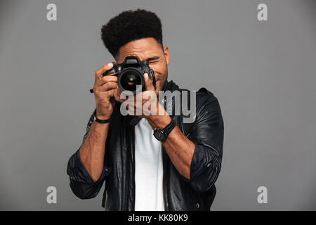 Schönen afrikanischen Kerl mit modischen Haarschnitt unter Foto Digitalkamera, auf grauem Hintergrund Stockfoto