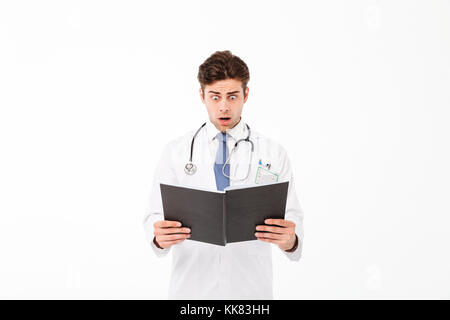 Porträt einer schockiert junge männliche Arzt mit Stethoskop in Uniform Holding ein Notebook gekleidet und beim Stehen und Schreien über Weiß bac isoliert Stockfoto