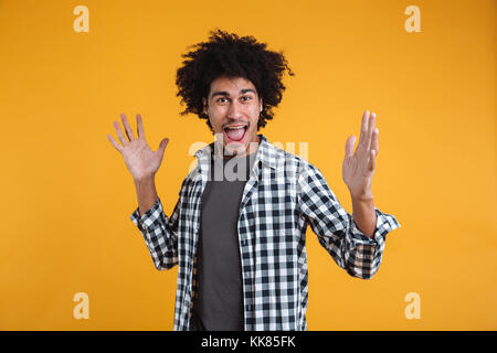 Porträt einer fröhlichen neugierige junge afro-amerikanische Mann schreien und Kamera über orange Hintergrund isoliert Stockfoto