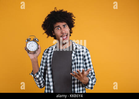 Portrait einer aufgeregt überrascht afrikanischen Mann mit Wecker über orange Hintergrund isoliert Stockfoto