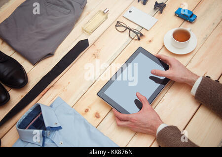 Ein Geschäftsmann mit einer Tablette. Das Konzept der Online Shopping für Männer. Modische Kleidung und Zubehör sind auf dem Tisch. Stockfoto