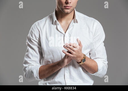 Zugeschnittenes Bild eines jungen Mann im weißen Hemd bekleidet und Tragen einer Armbanduhr über grauer Hintergrund Stockfoto