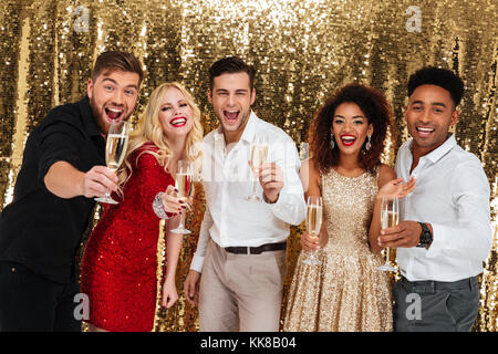 Portrait Of Happy aufgeregt multirassischen Gruppe von Freunden feiern gemeinsam halten Sektgläser über golden glänzenden Hintergrund isoliert Stockfoto